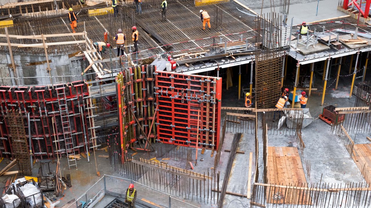 Chantier de construction industrielle avec des travailleurs en vêtements de haute visibilité près d'une structure en acier.