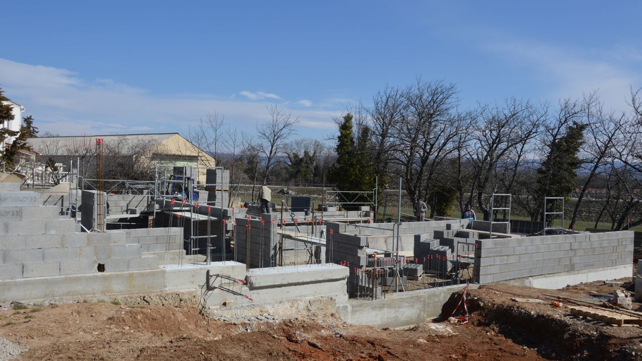 Chantier extérieur montrant des murs en blocs de béton et des échafaudages sous un ciel dégagé.