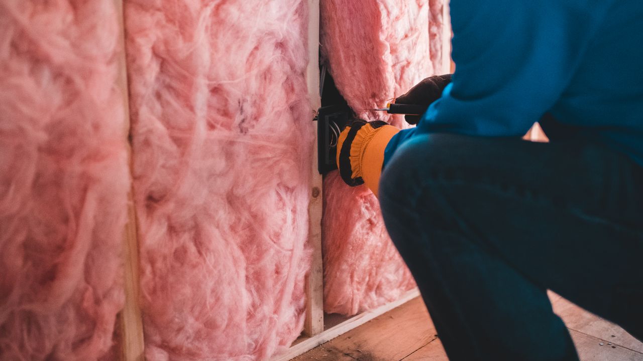 Travailleur concentré installant une isolation en fibre de verre rose à l'intérieur d'un bâtiment.
