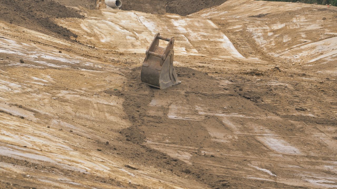 Godet de pelleteuse sur un chantier extérieur avec de la terre et des équipements.