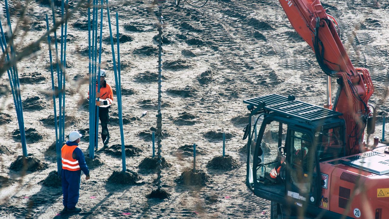 Un chantier de construction avec des travailleurs et une excavatrice forant des trous dans le sol.