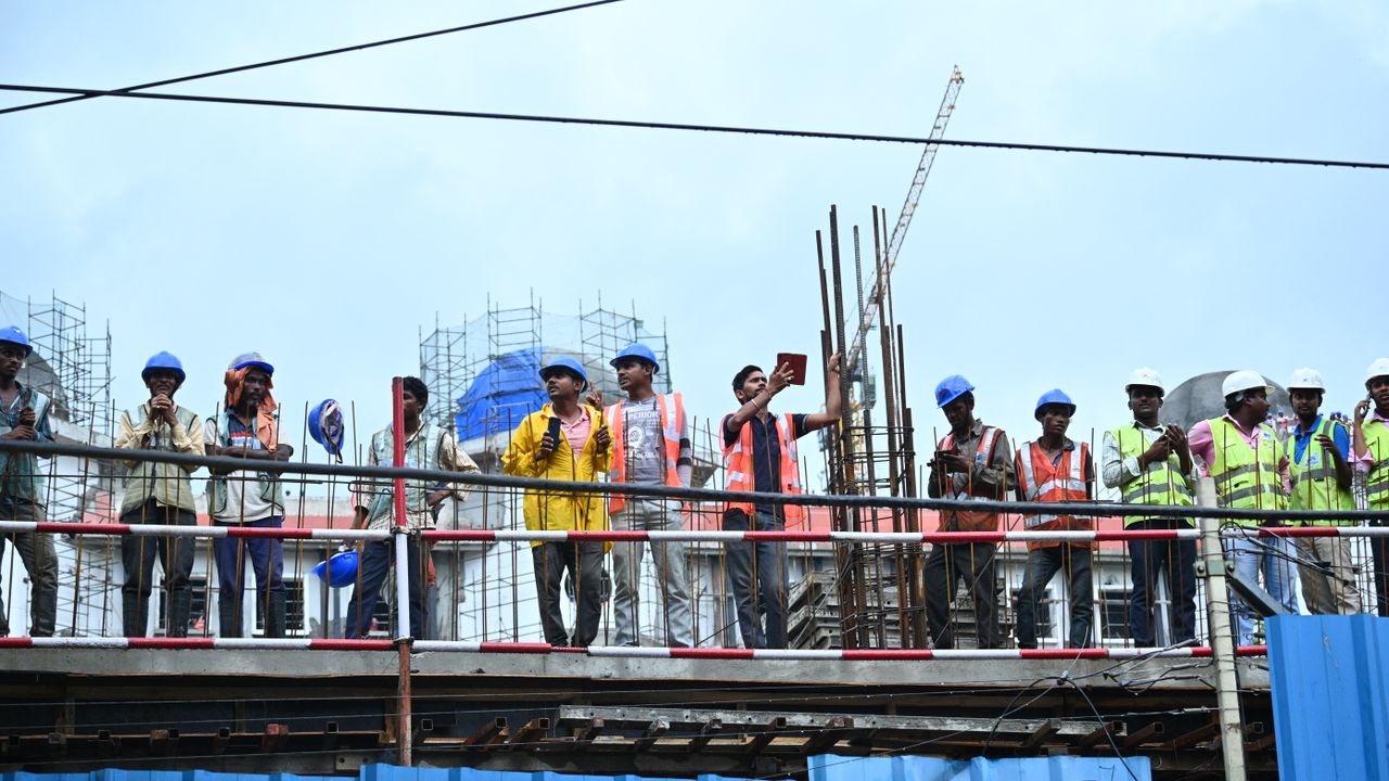 Groupe de travailleurs de la construction sur un échafaudage portant des équipements de sécurité, des casques et des gilets.
