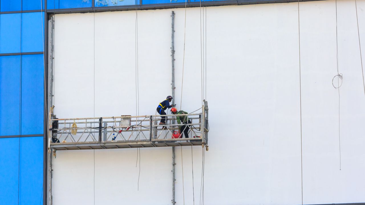 Deux ouvriers du bâtiment sur un échafaudage réparant et peignant une façade de bâtiment.