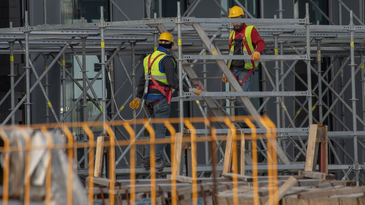 Deux travailleurs de la construction portant des équipements de sécurité et des casques travaillant sur un échafaudage en extérieur.